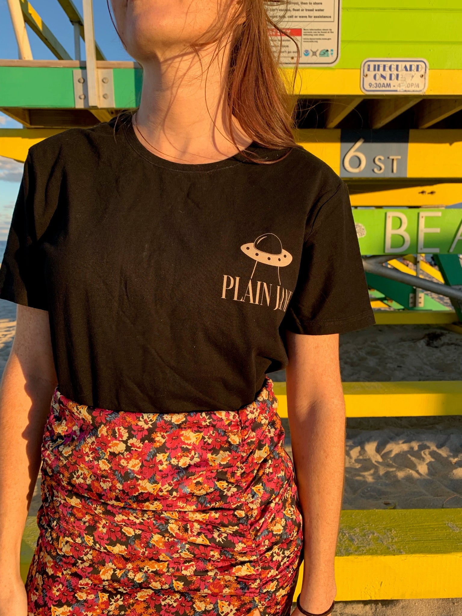 Person wearing a Plain Jane shirt in front of colorful architecture