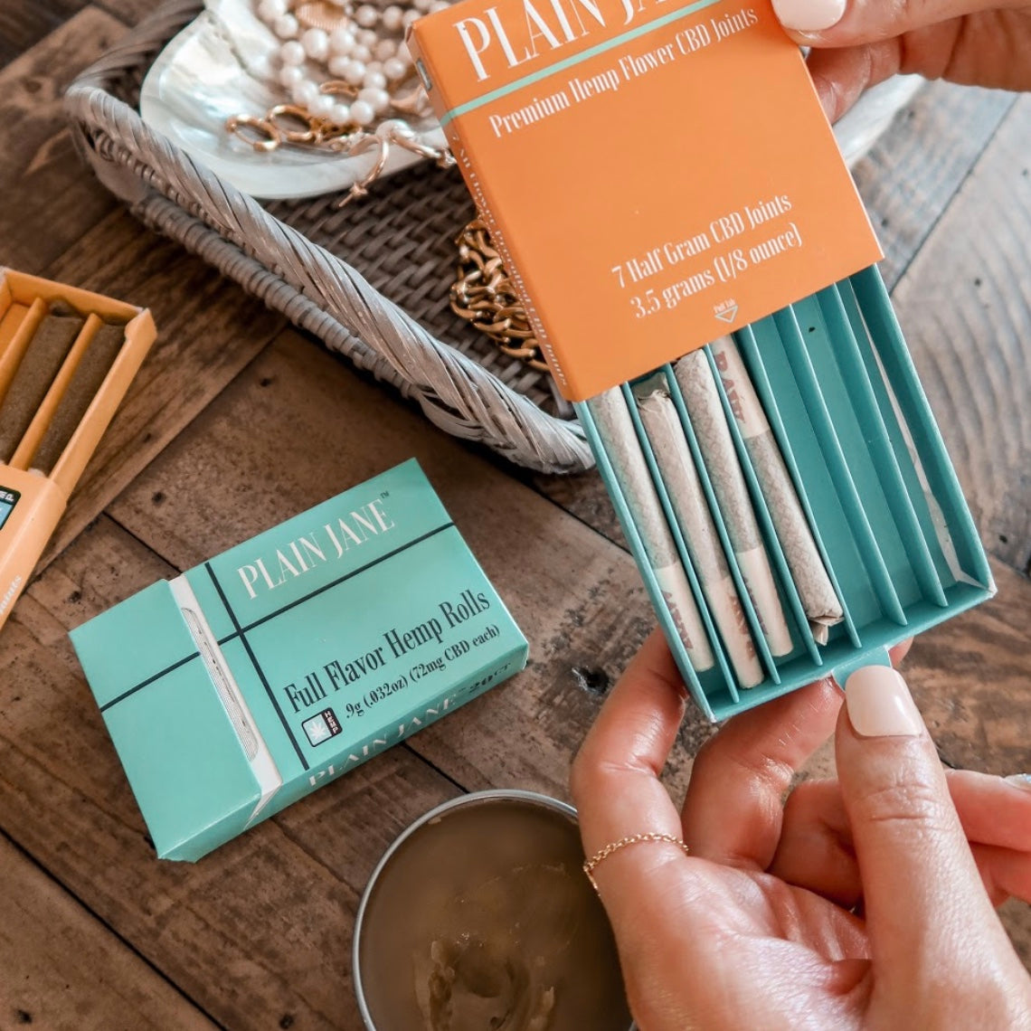 Hands opening Plain Jane hemp rolls and CBD joints on a tabletop