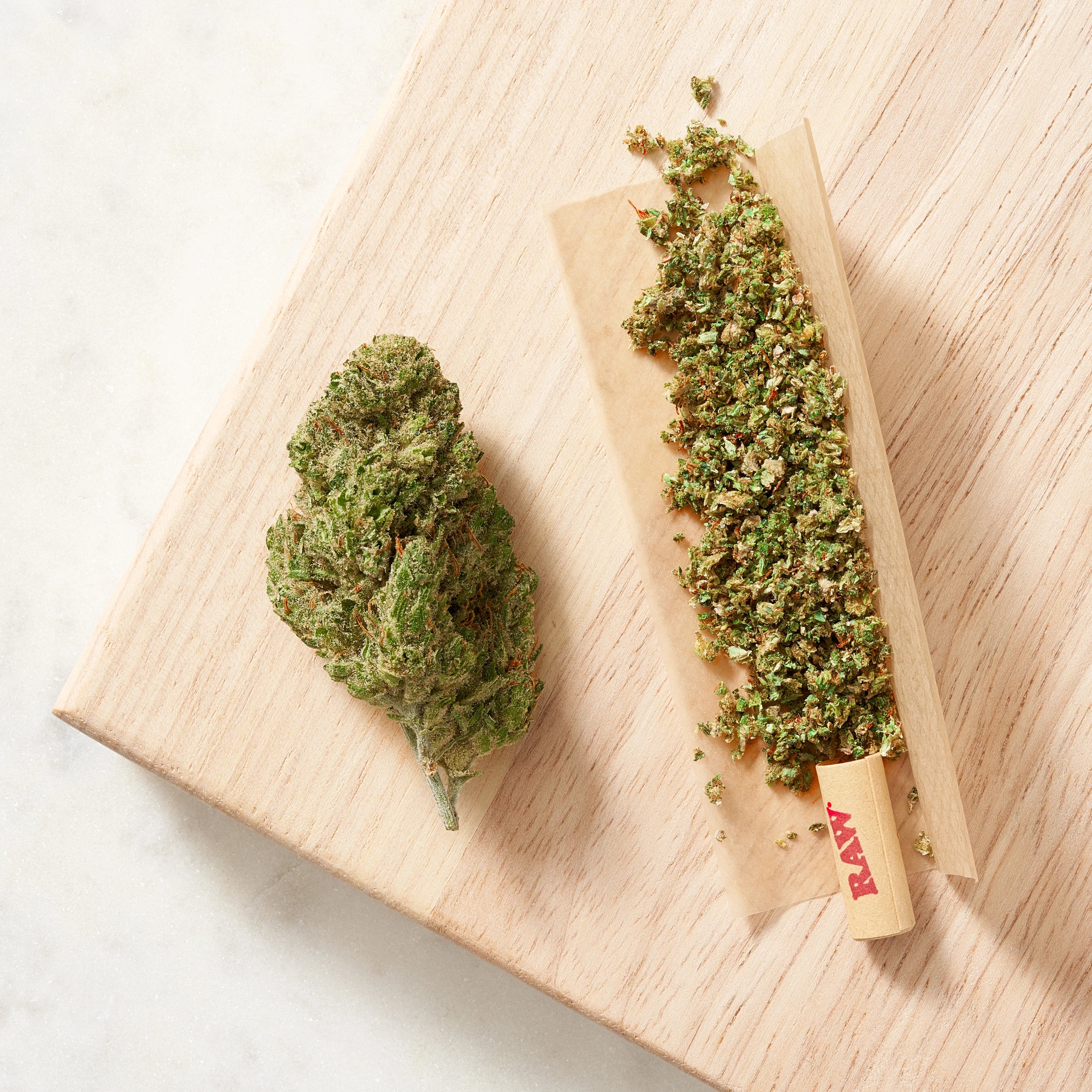 Photographed cannabis flower and loose flower beside rolling paper on a light wooden board